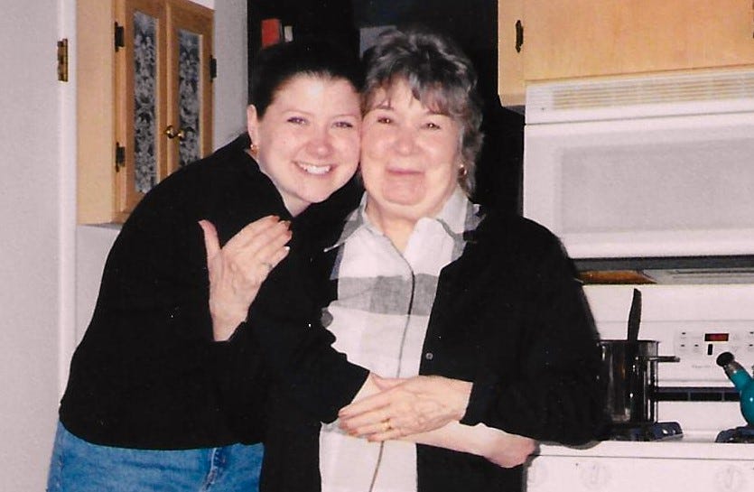 Patty with Rose in Rose's kitchen, embracing from the side, both facing the camera and smiling