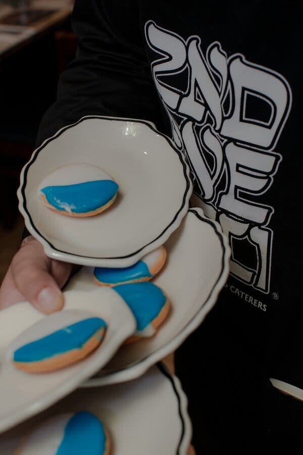 A hand holds several white plates with blue and white cookies on them.