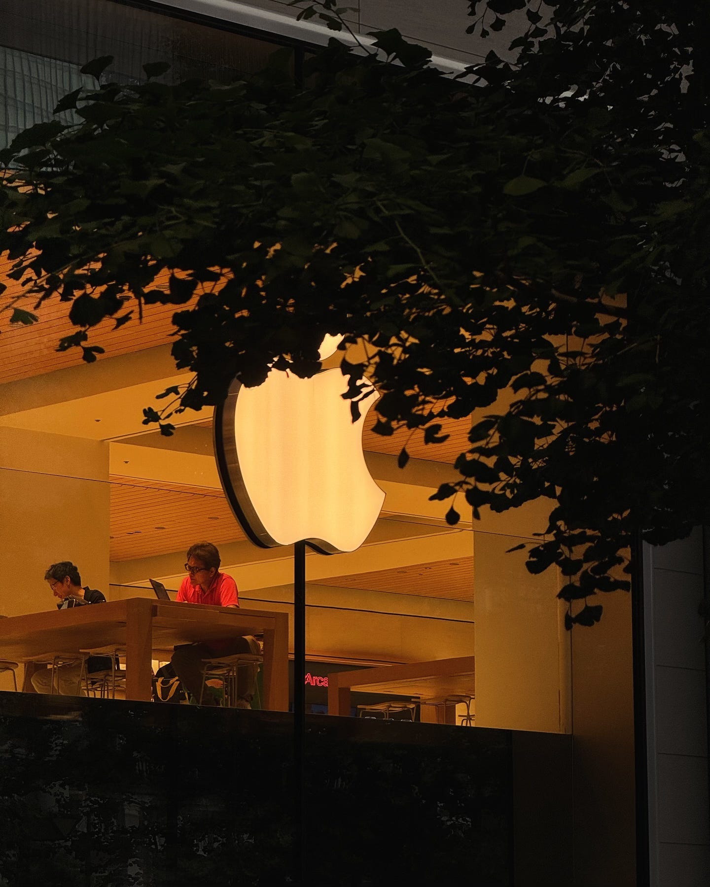 The upper level of Apple Marunouchi, pictured from the street. Two people sit at a table behind the Apple logo.