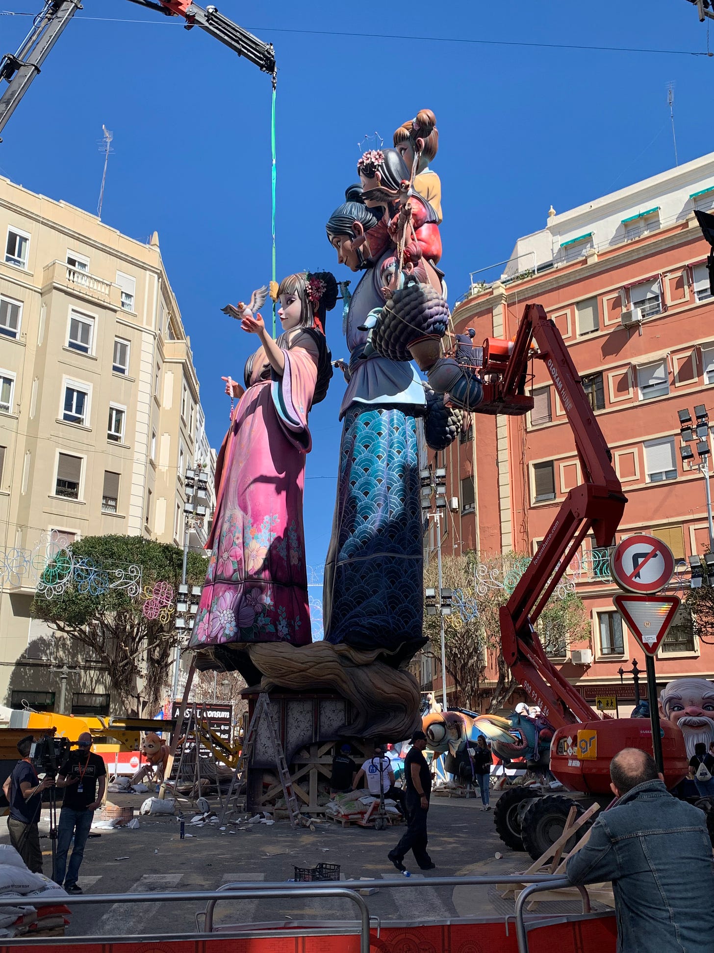 A crane lifts part of a giant Falla into place while staff on a cherry picker works on another section, high above the ground