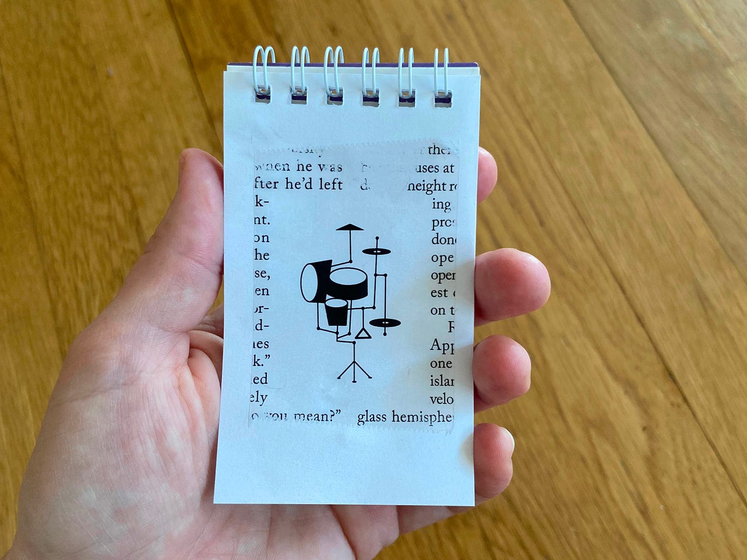 A hand holding a notepad of white paper sheets and the tape with the drumset image stuck to it