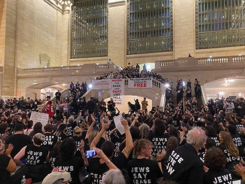 Jewish Voice for Peace NYC action at Grand Central Station. Many people are pictured with shirts that say ''Ceasefire now''