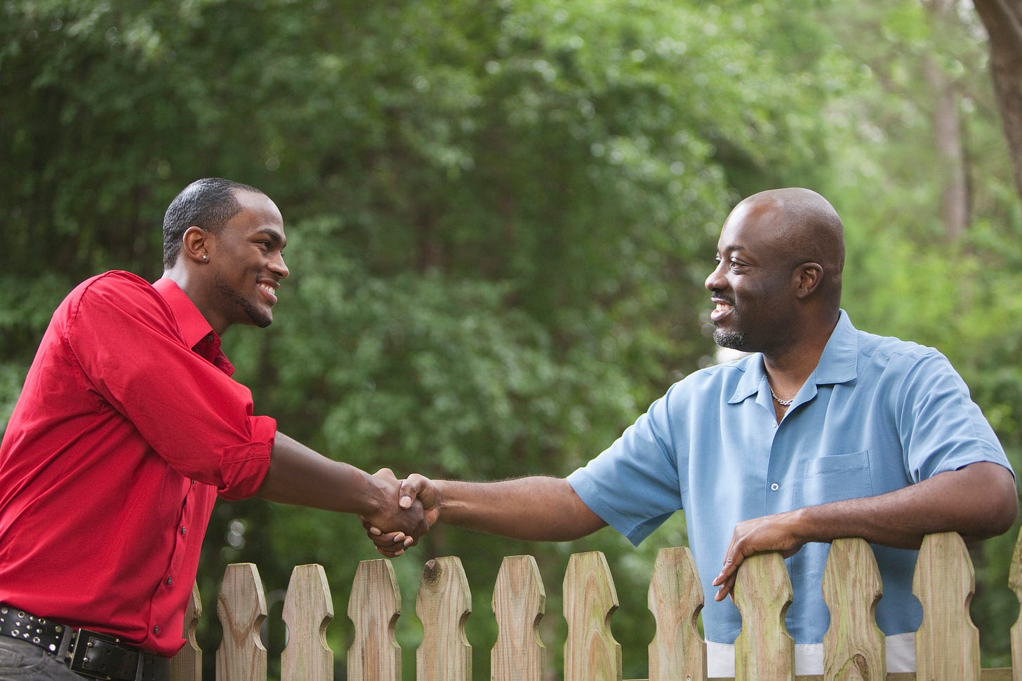 Two men shake hands over a fence.
