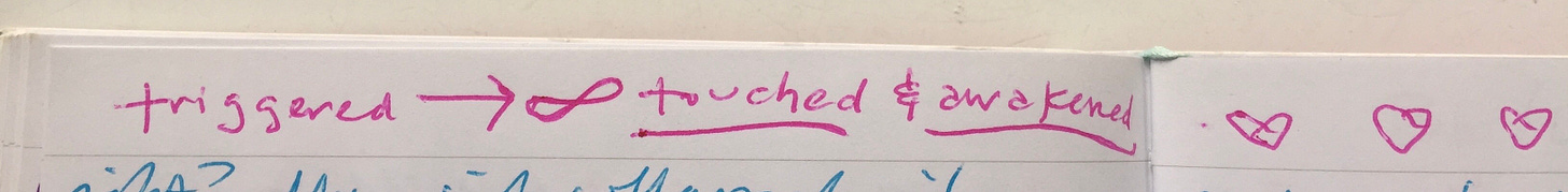 The top of a journal page has writing in hot pink ink which reads “triggered—> ♾️ touched & awakened” with a few hearts drawn next to it onto the other page.