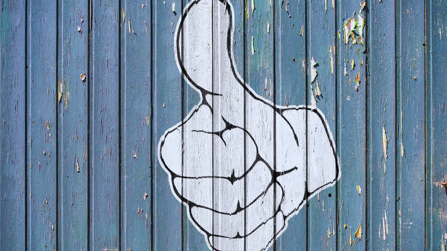 Black and white thumbs-up painted on a blue, wooden fence fraying and peeled with time.