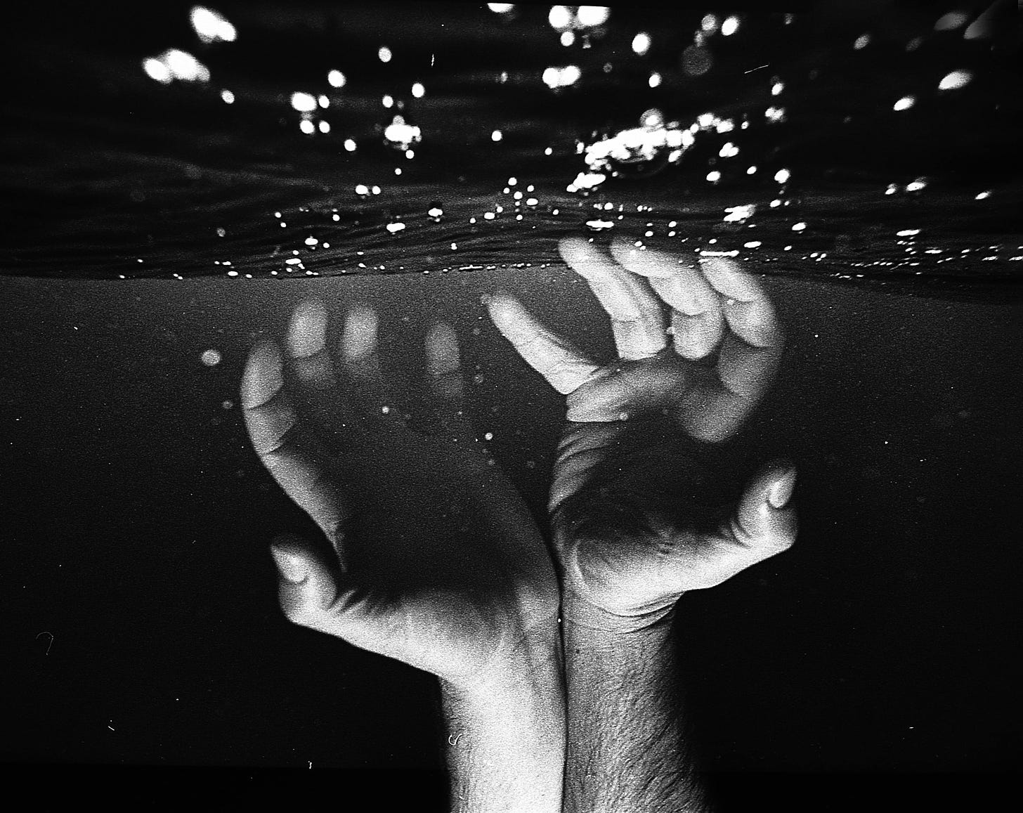 Black and white photo of hands under water reaching for the top.