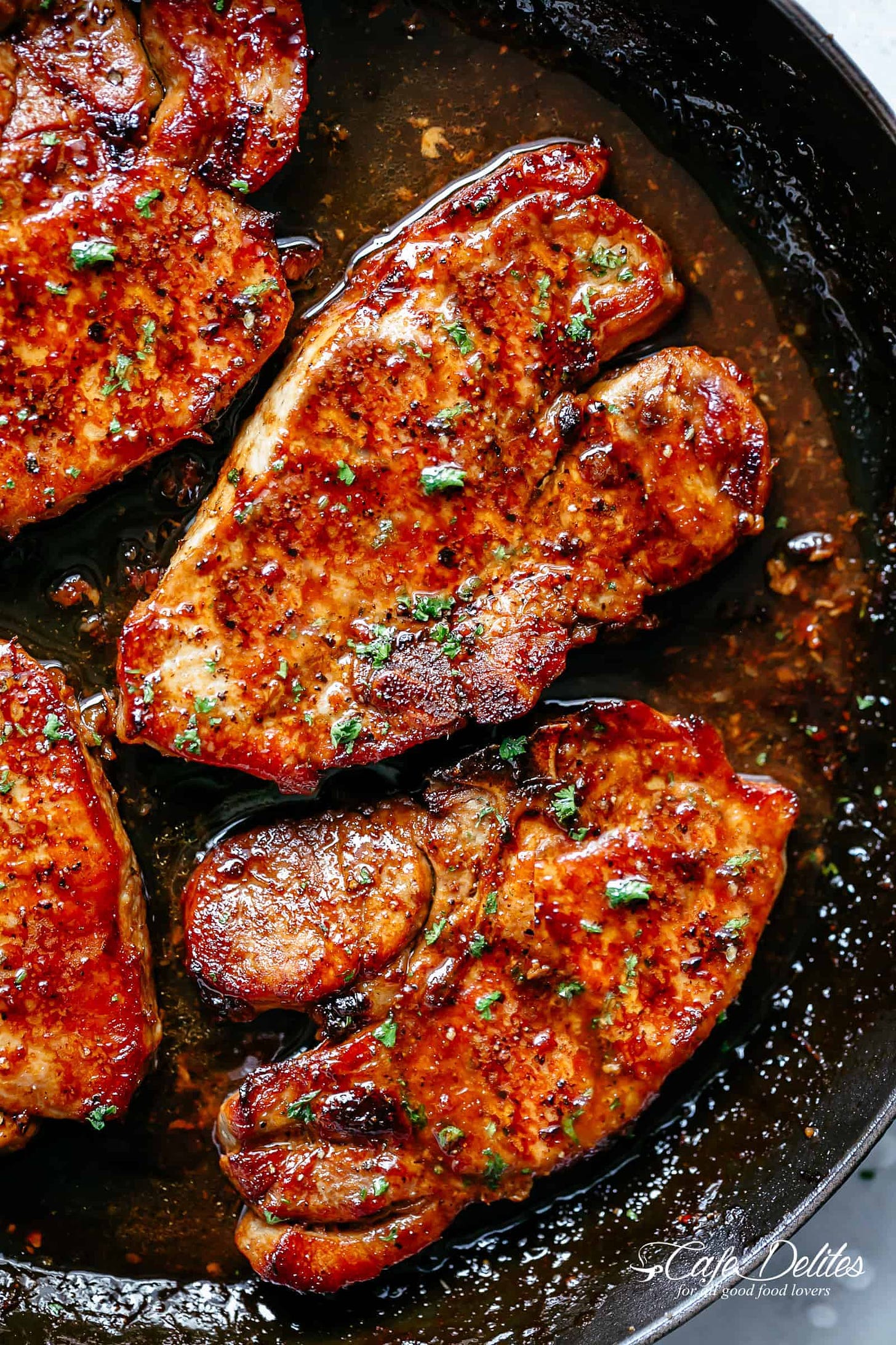 Four honey garlic pork chops in frying pan with green herbs sprinkled on top.