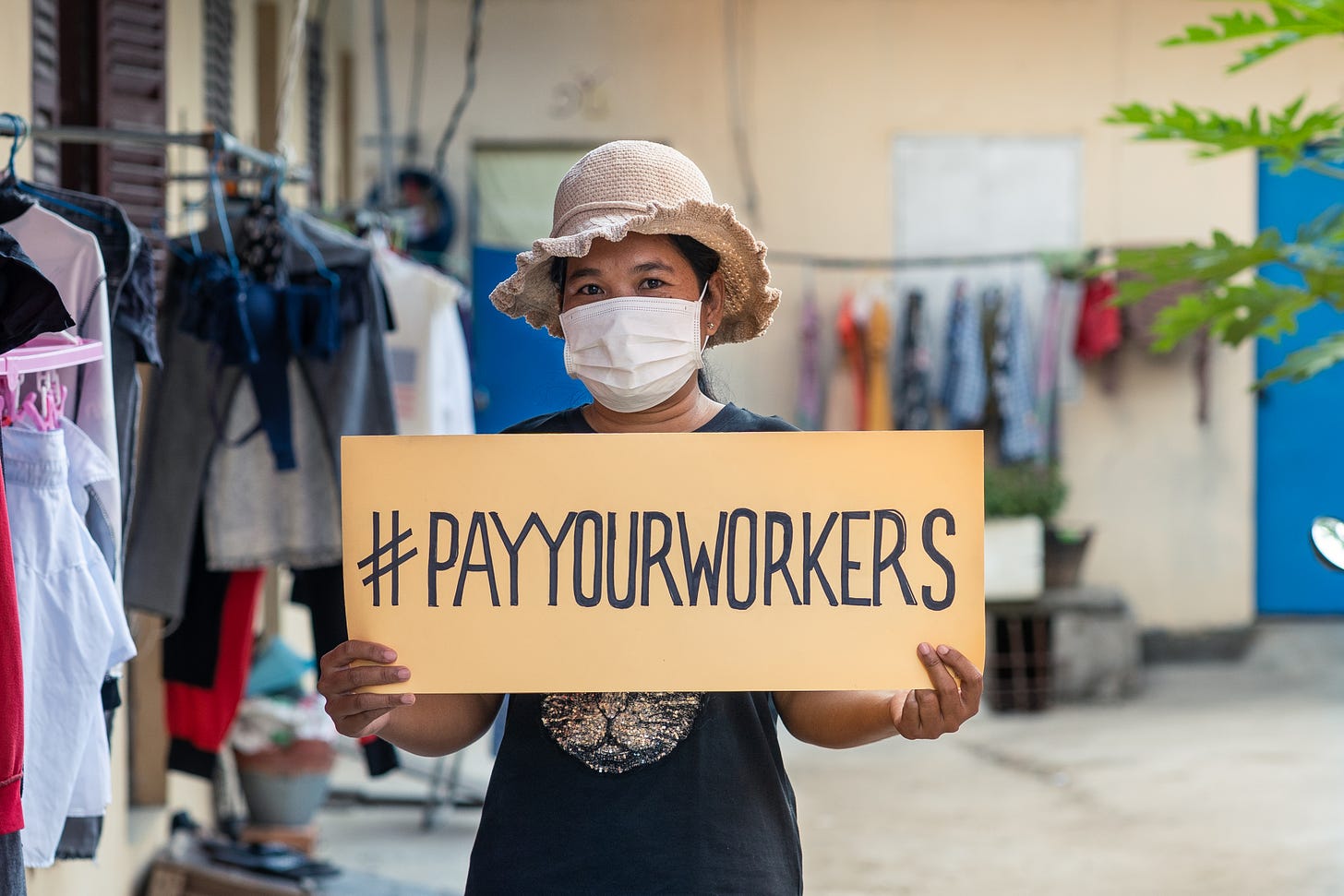 A female Cambodian garment worker wearing a face mask holds up a sign saying #PayYourWorkers in reference to the international campaign.