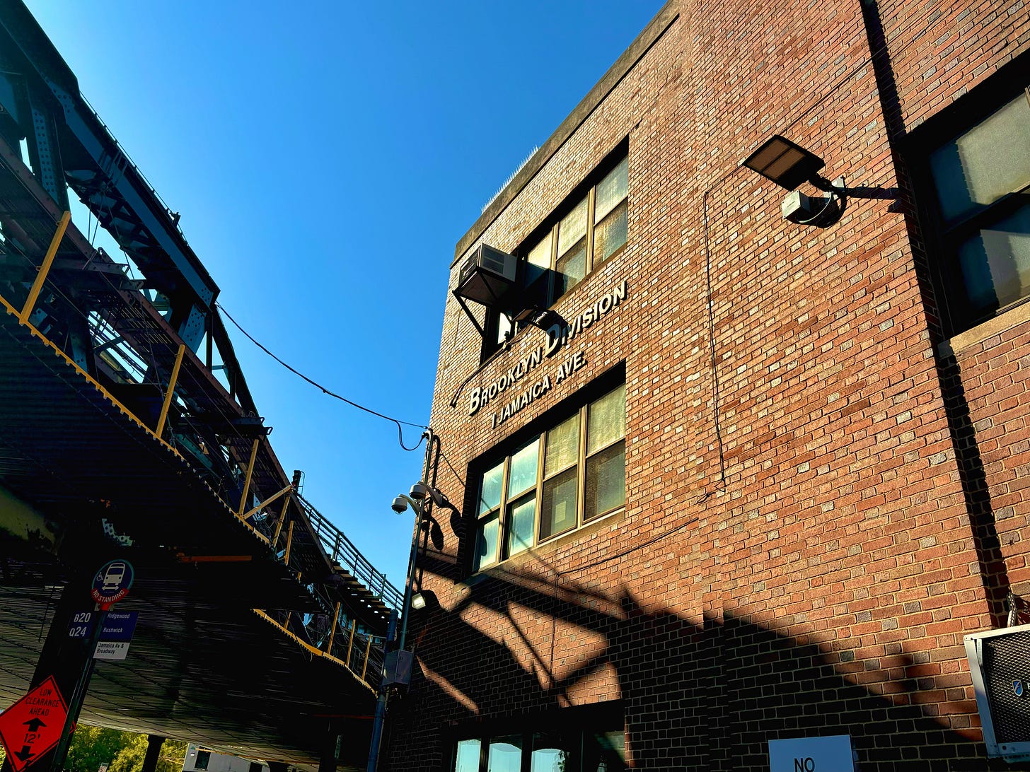 A large brick building labeled Brooklyn Division/Jamaica Ave across from an elevated train rail.