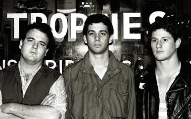 A black and white photograph of the band, the Minutemen. Pictured from left to right: D. Boon, Mike Watt, and George Hurley. Photo by Martin Lyon.