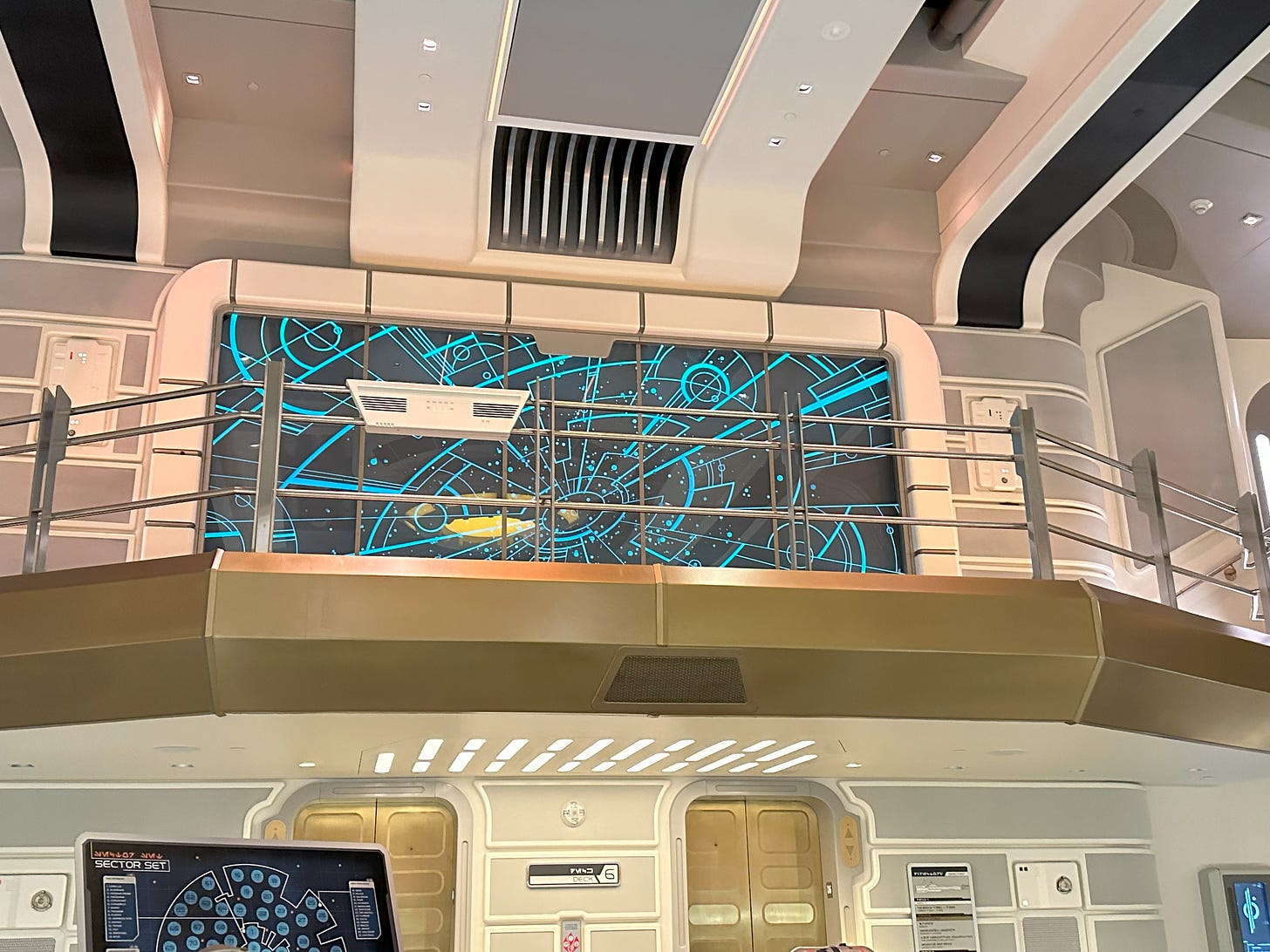 Atrium of the Halcyon starcruiser, with an upper level with silver railings, behind it a star map of the galaxy