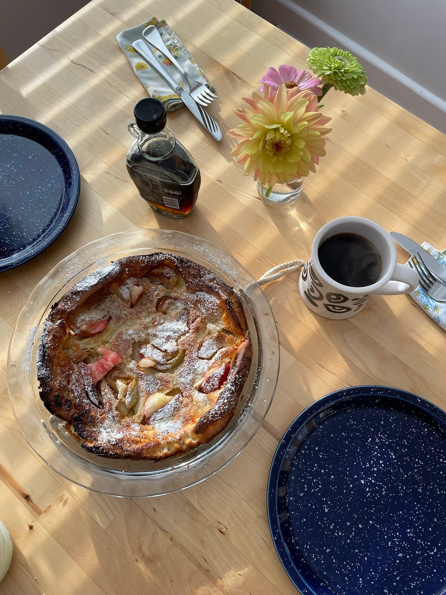 Overhead shot of a dining table with filter coffee, an apple dutch baby, plates, cutlery and maple syrup.