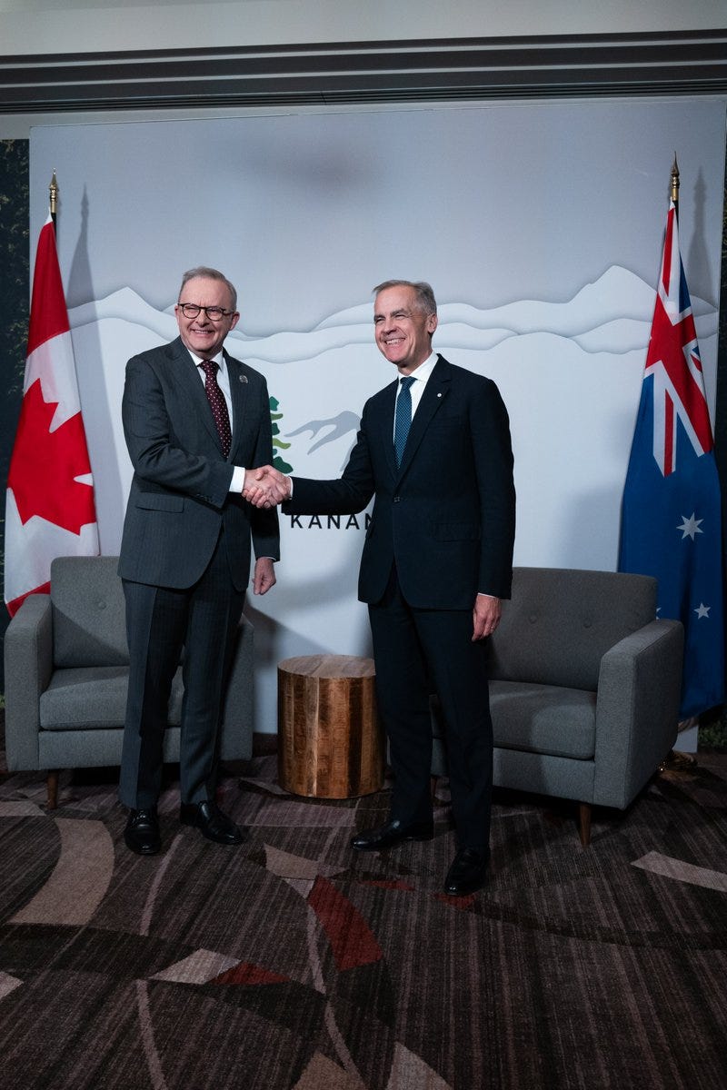 Prime Minister Mark Carney is standing next to the Prime Minister of Australia, Anthony Albanese, shaking hands. The G7 Kananaskis Leaders’ Summit logo is seen on a backdrop behind the leaders, situated between the Canadian and Australian flags.