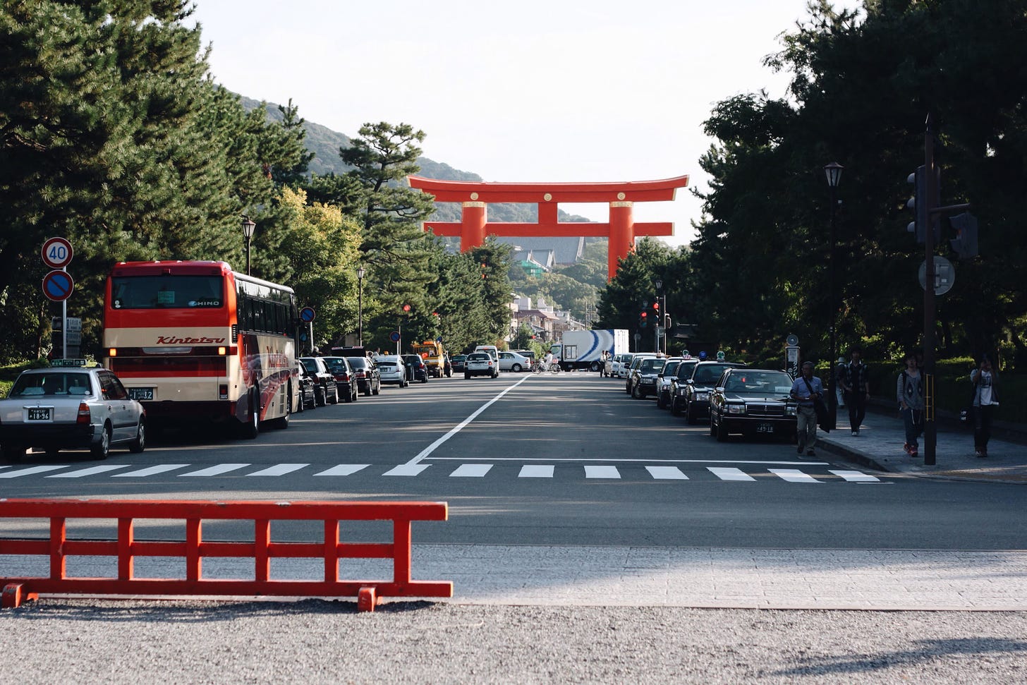 A Kyoto street lined with cars and a red gate in the background.