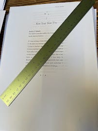 A printed manuscript, with the opening paragraph on show. There is a metal ruler across it, partially obscuring the words. The page starts with Chapter 1. New Year, New You.