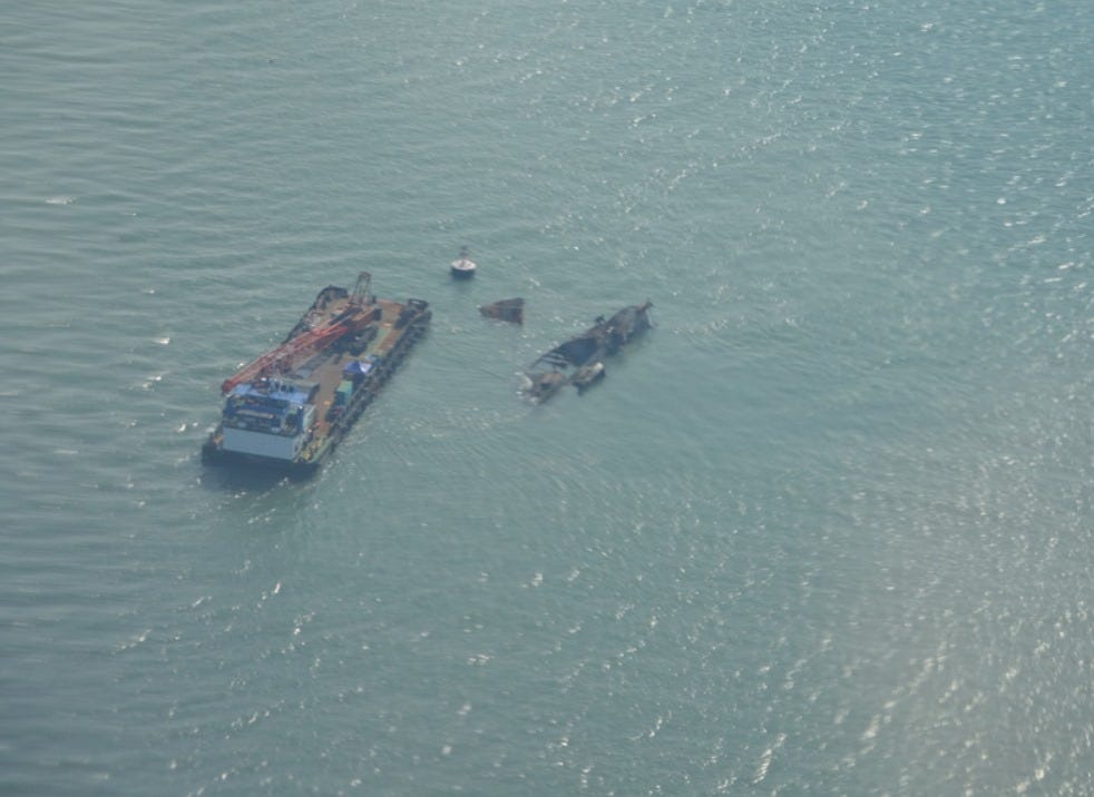 A barge on open water, from above, with a small boat beside it and a buoy