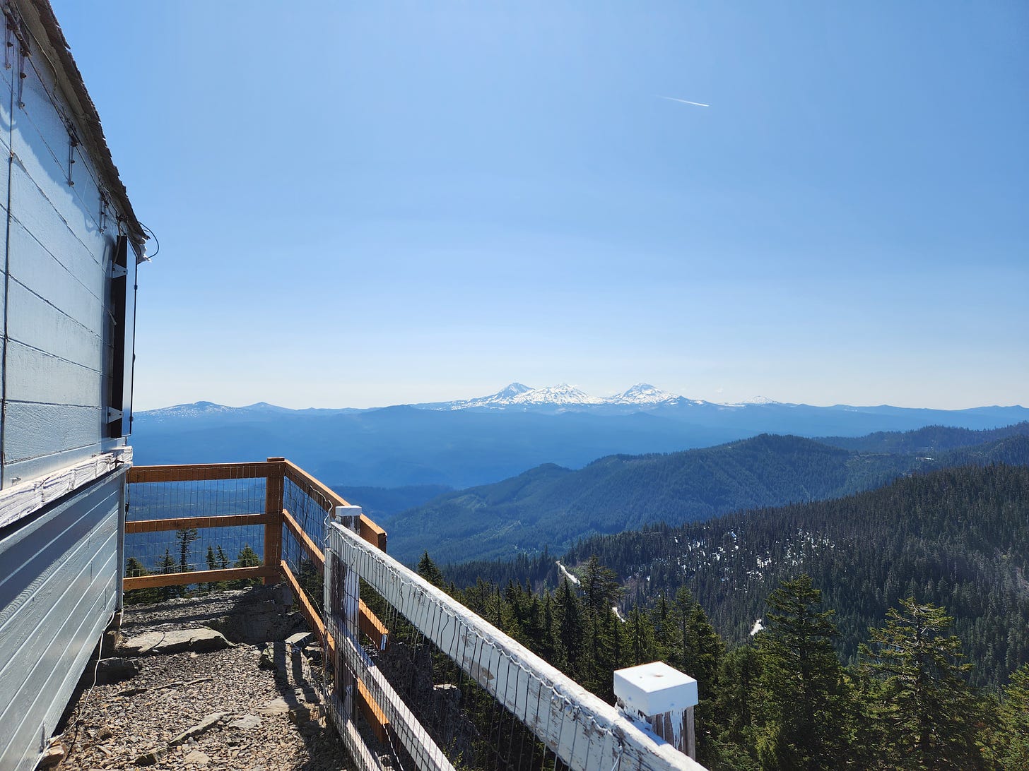 edge of white lookout building with snow-covered mountains in teh distance, forests in between