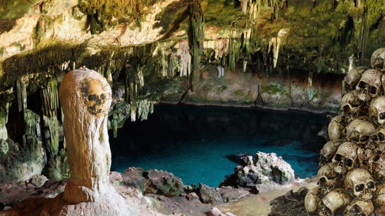 A pile of skulls form an archway that overlooks a broad expanse of water inside an enormous cavern