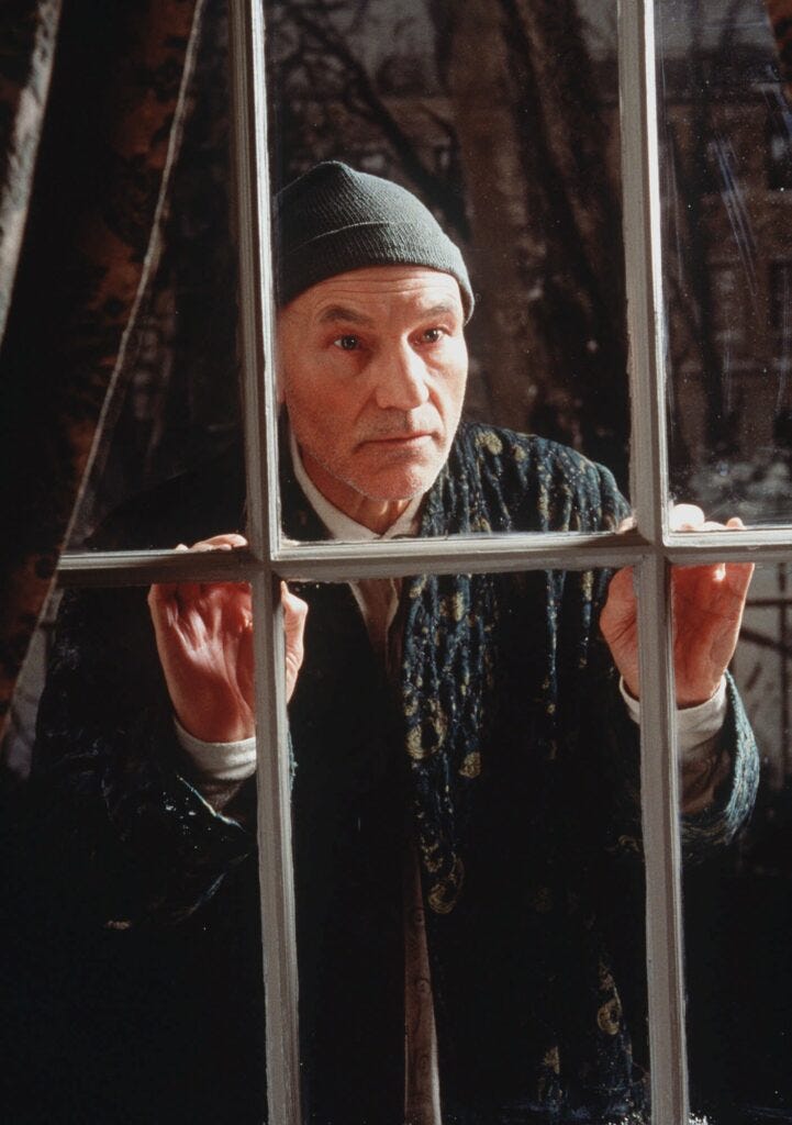 Patrick Stewart as old Ebenezer Scrooge, wearing a knit cap and staring out a window.
