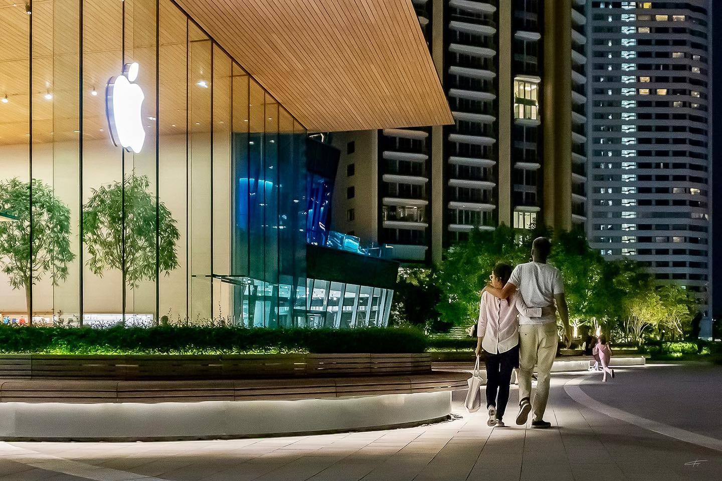 Two people walk together past Apple Iconsiam in the early evening.