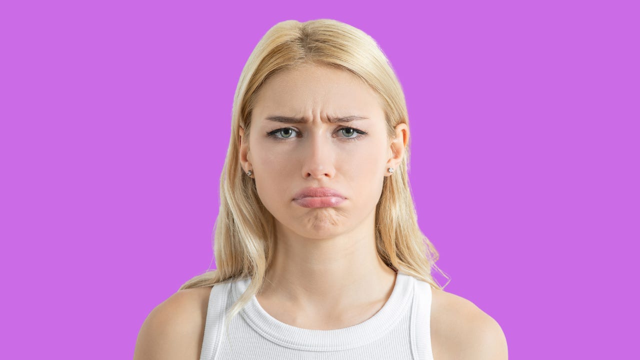 A disappointed blonde girl in front of a pink background.