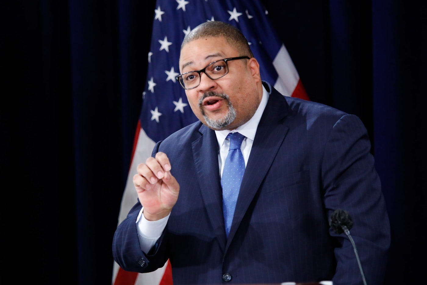 Manhattan District Attorney Alvin Bragg speaking at a press conference, with the U.S. flag in the background. Bragg is gesturing as he discusses legal matters related to the 34 felony convictions of former President Donald Trump and the debate over presidential immunity.