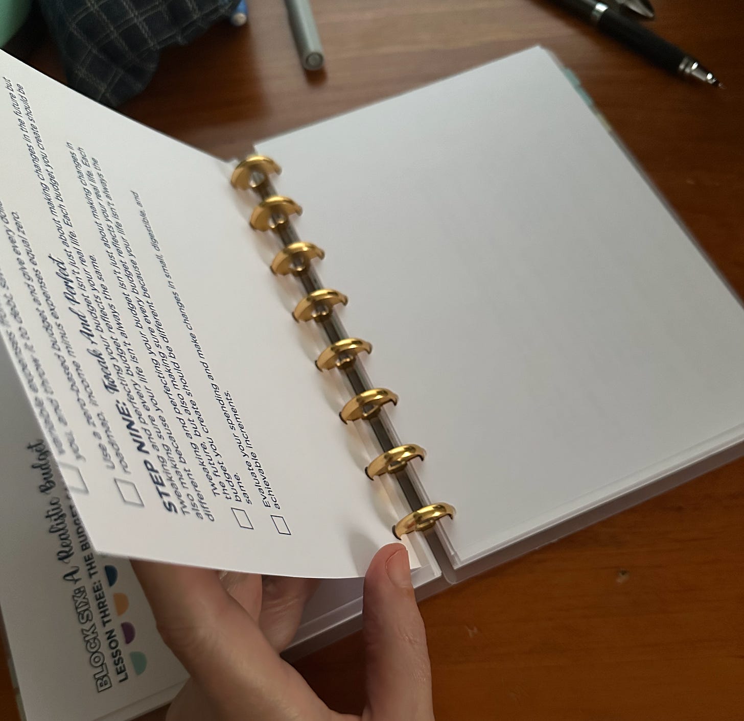 A5 notebook bound with 8 gold aluminium discs is on a wooden desk. A hand is holding the left hand side page up, revealing that one side of each page is A4 paper printed on one side only, cut in half.