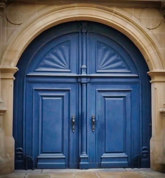A large bright blue double door of an old stone building with intricate designs and silver handles