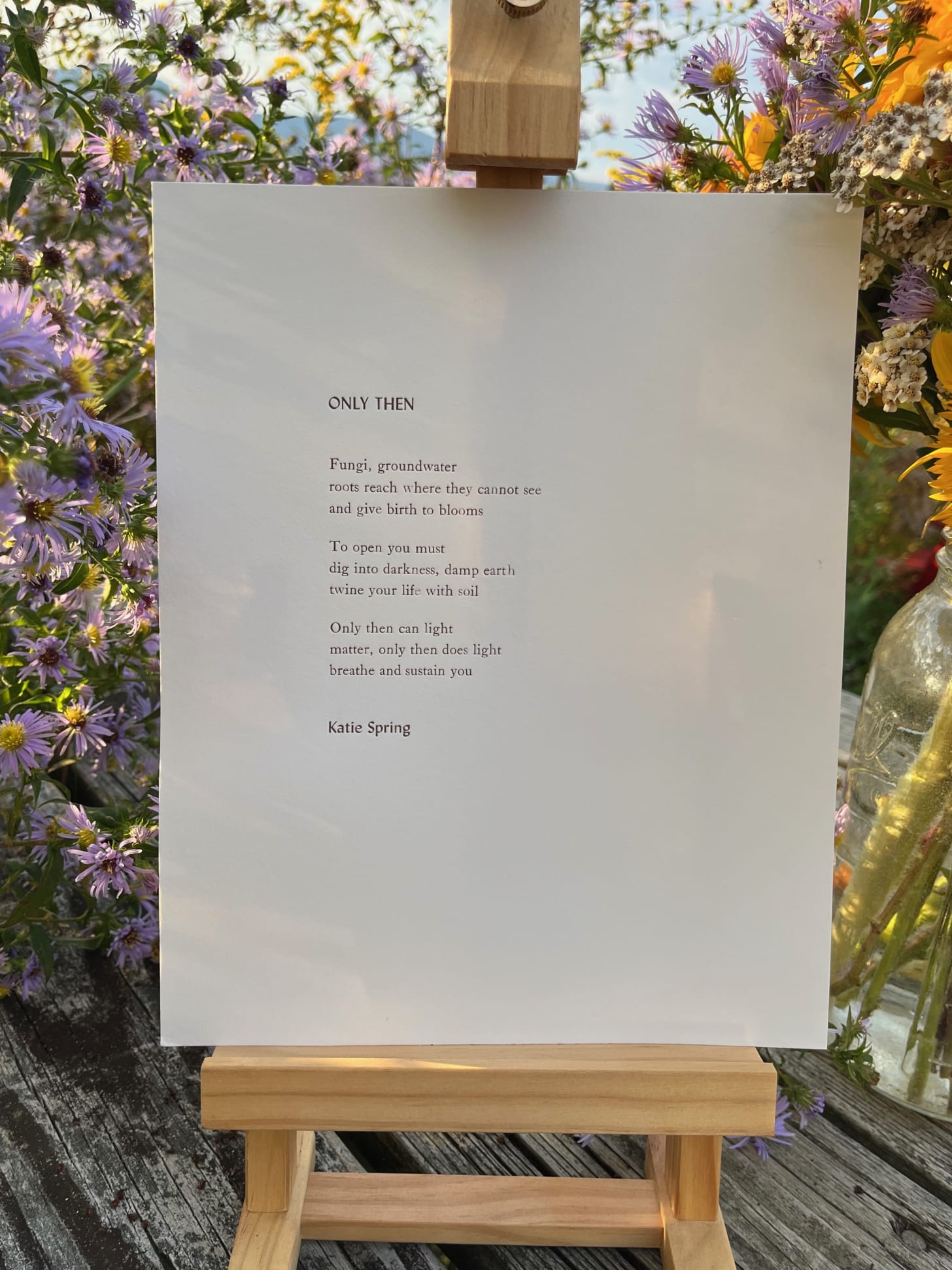 A letterpress poem titled "Only Then" by Katie Spring, on a wooden stand with flowers framing it.