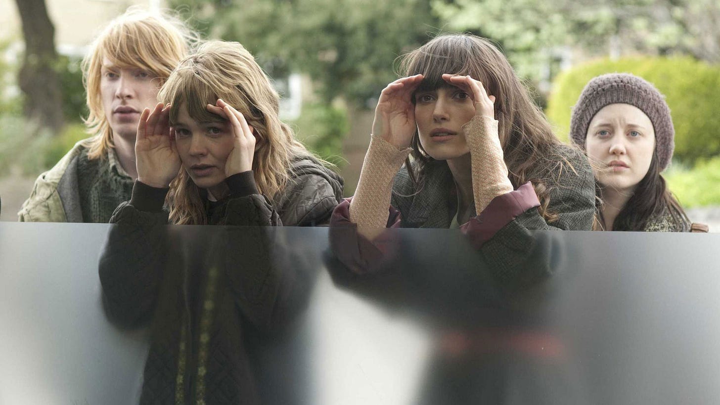 Still from Never Let Me Go, which shows Kathy and Ruth peering in through a window with a couple behind them