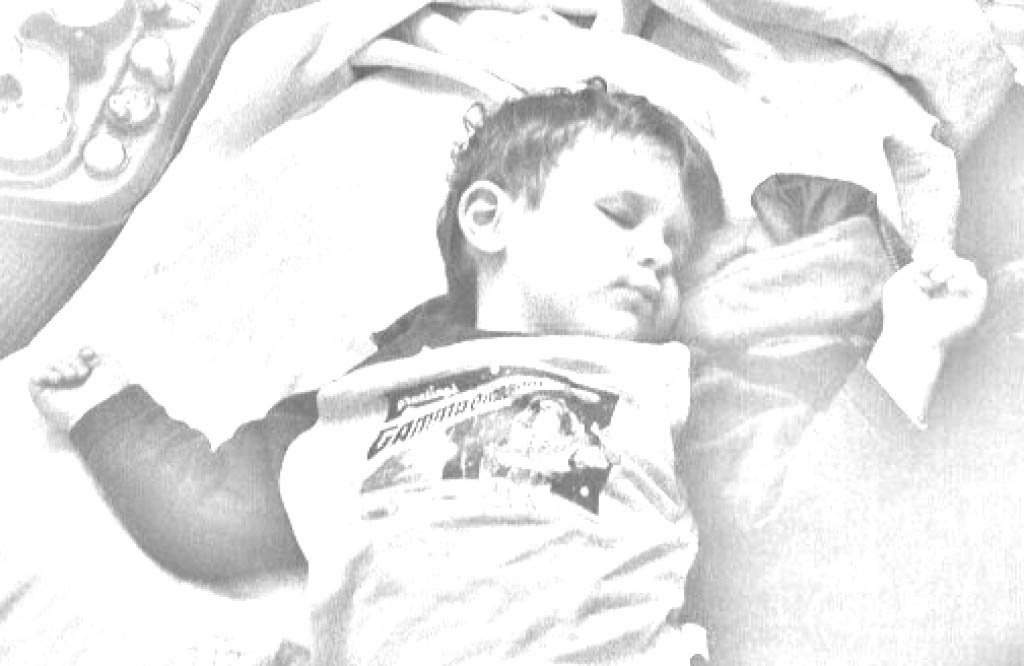 A black and white image of a young child flopped back onto some pillows and blankets. They are deeply asleep.