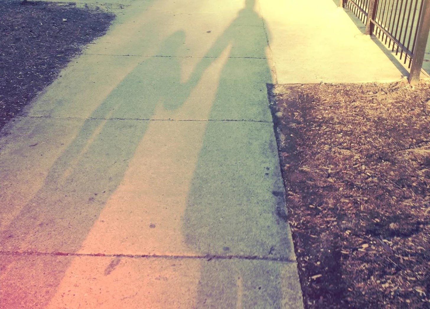 Mother and child holding hands in shadow on sidewalk.