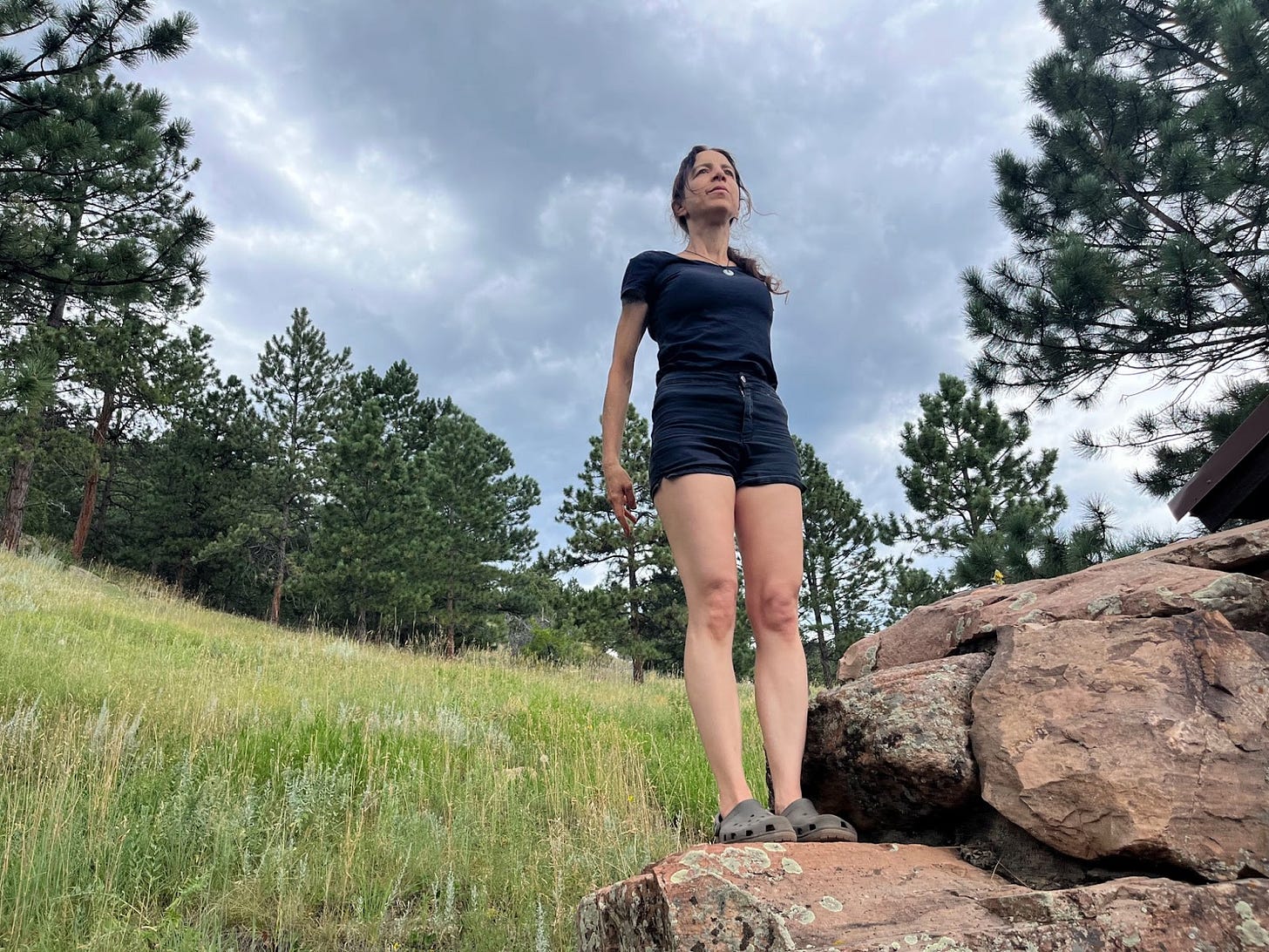 the author standing in mountain pose on a rock amongst prairie grasses and trees.