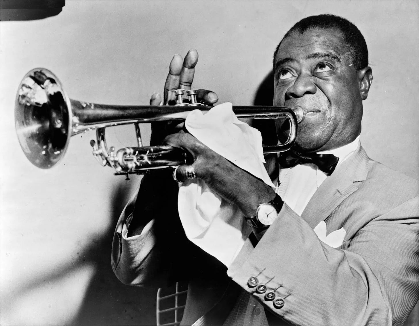 Louis Armstrong rolling his eyes while playing the trumpet, holding a handkerchief in his left hand