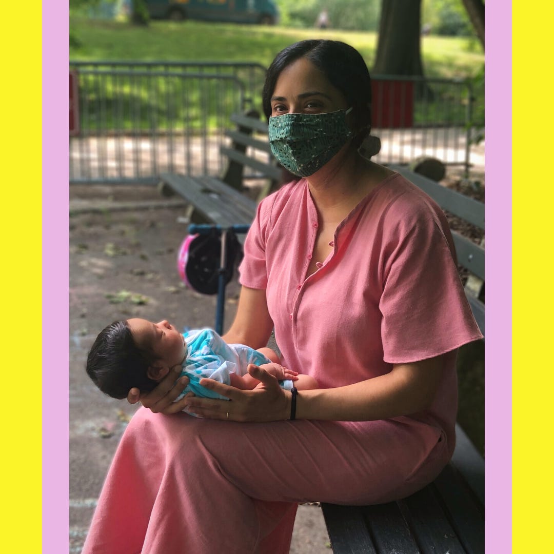 The author, a Latina mother with black hair, sitting on a park bench with a green cloth face mask, holding her newborn baby in her lap.