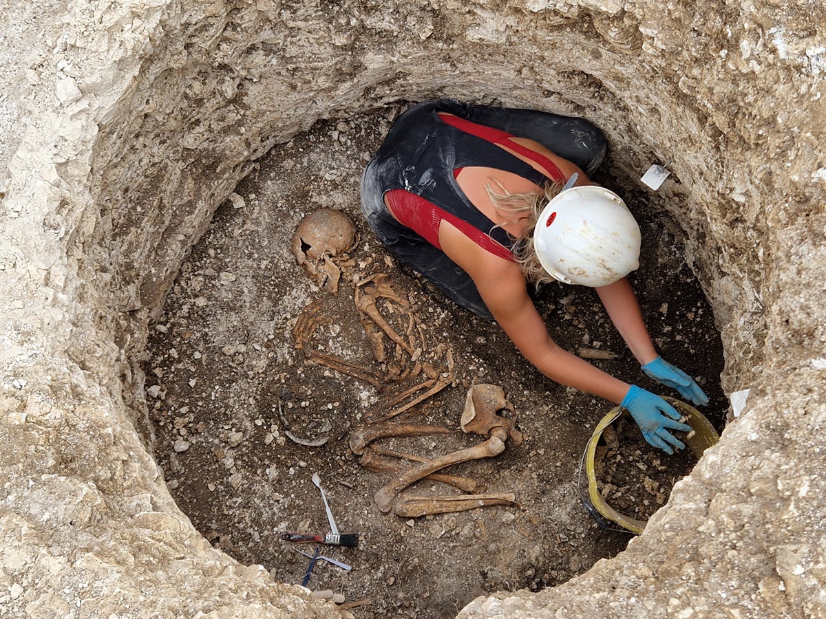 A woman archaeologist in a circular burial pit featuring a skeleton A woman archaeologist in a circular burial pit featuring a skeleton