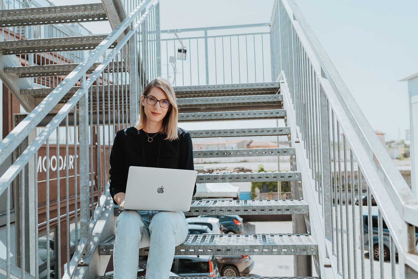 Lilli sitting on the stairs with a laptop and looking in the camera