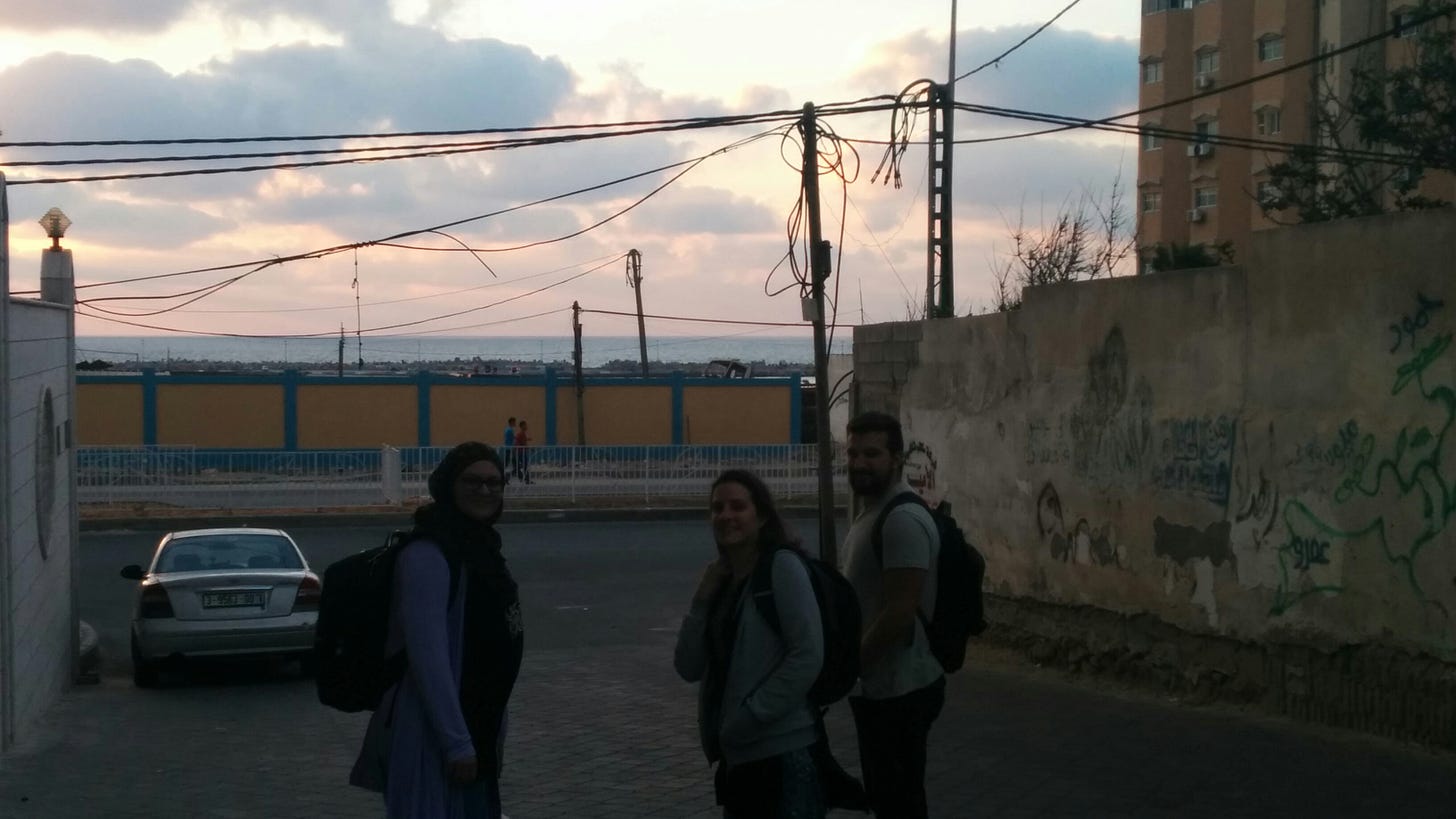 Three people smile at the camera on a driveway outside an office building at sunset