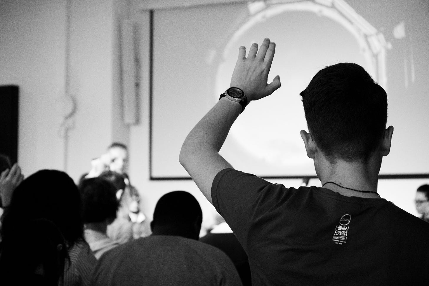 Photo of the back of a man holding up his hand in a lecture hall