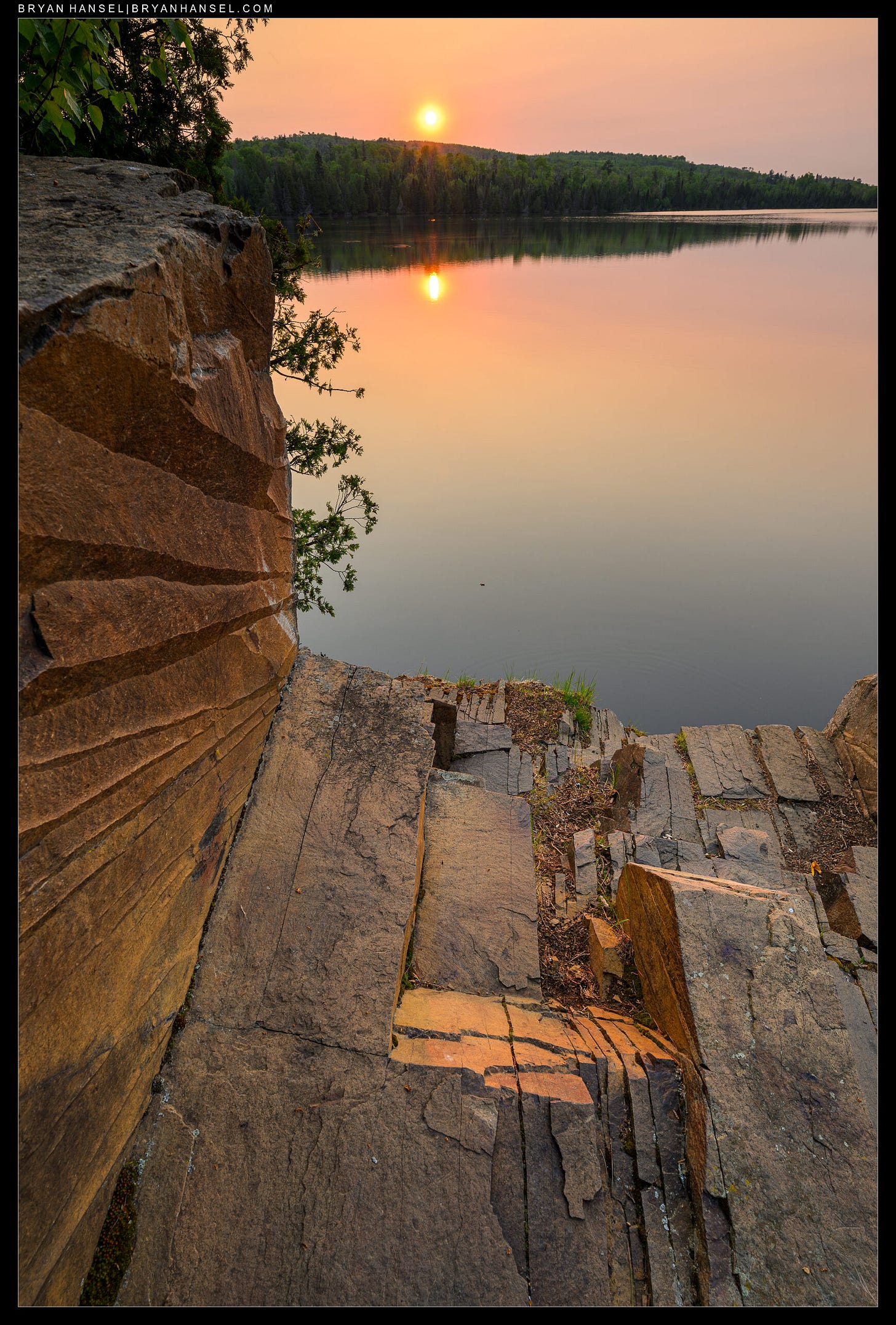A photo of an orange sky and orange rocks and orange lake from teh wildfire smoke.