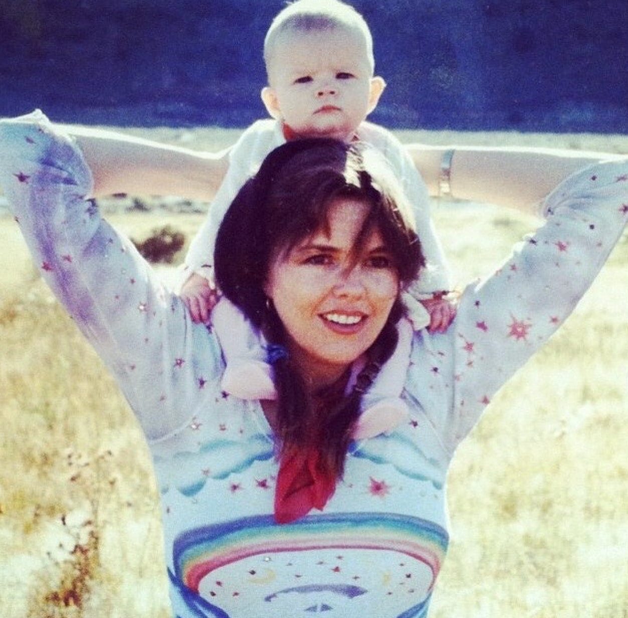 Amber as a baby, sitting on her mother's shoulders. They are in a field. 