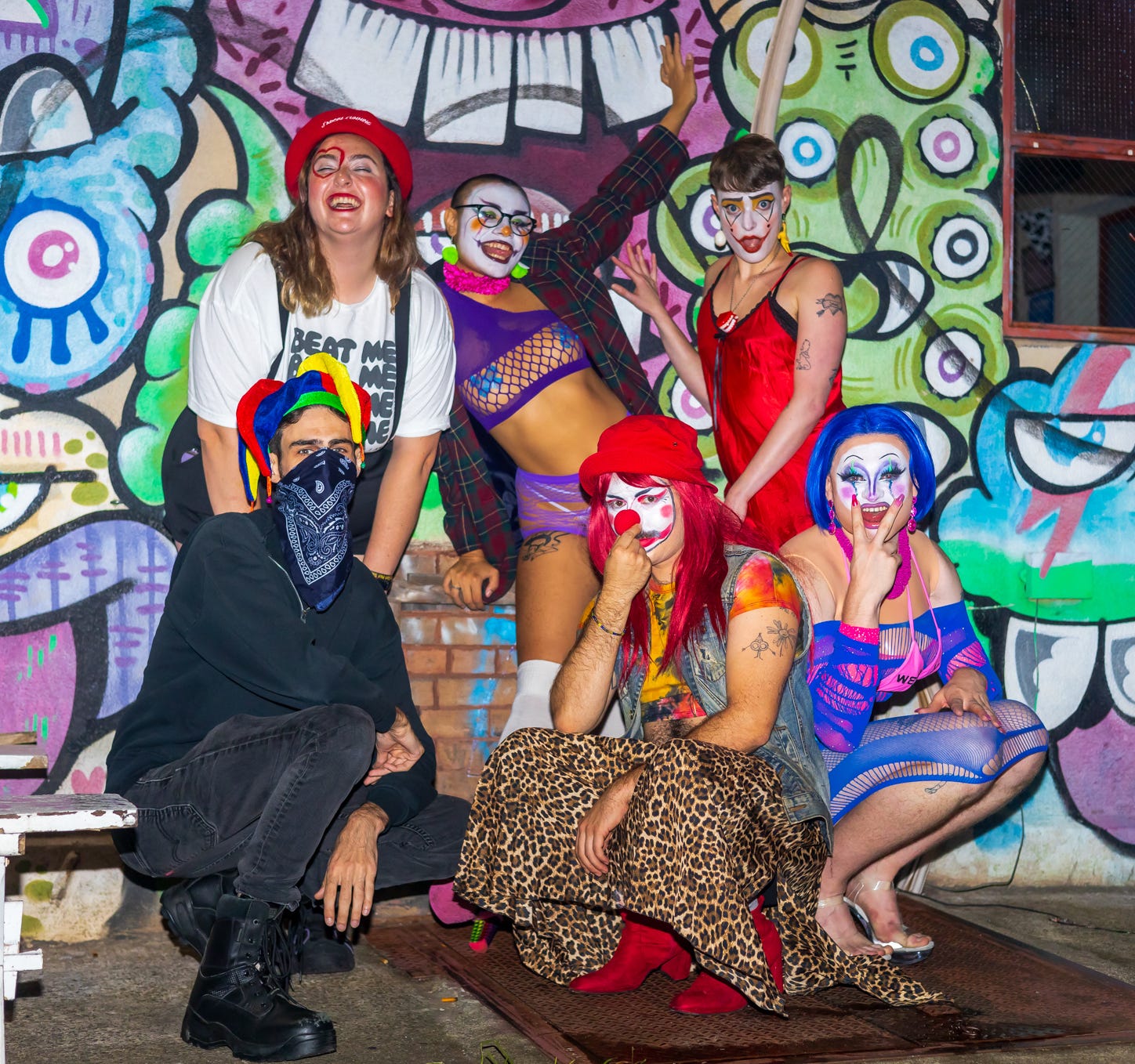 Caty, Cochina Divina, Cassidy Dawn Graves, Jester of No Court, Babz, and Tank pose in clown outfits in front of colorful wall mural outside queers n peers variety show