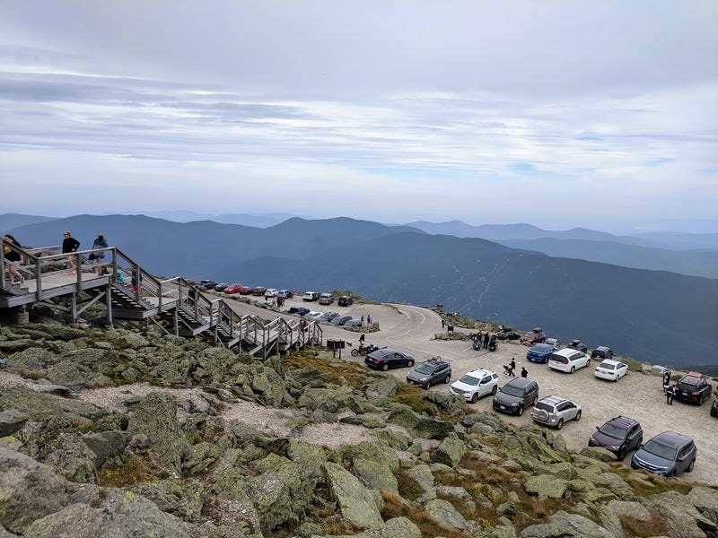 The Mt Washington parking lot for the auto road, with twenty cars visible and people walking up a wooden stairway