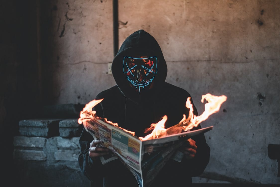 Free Person with Black Mask holding a Burning News Paper Stock Photo