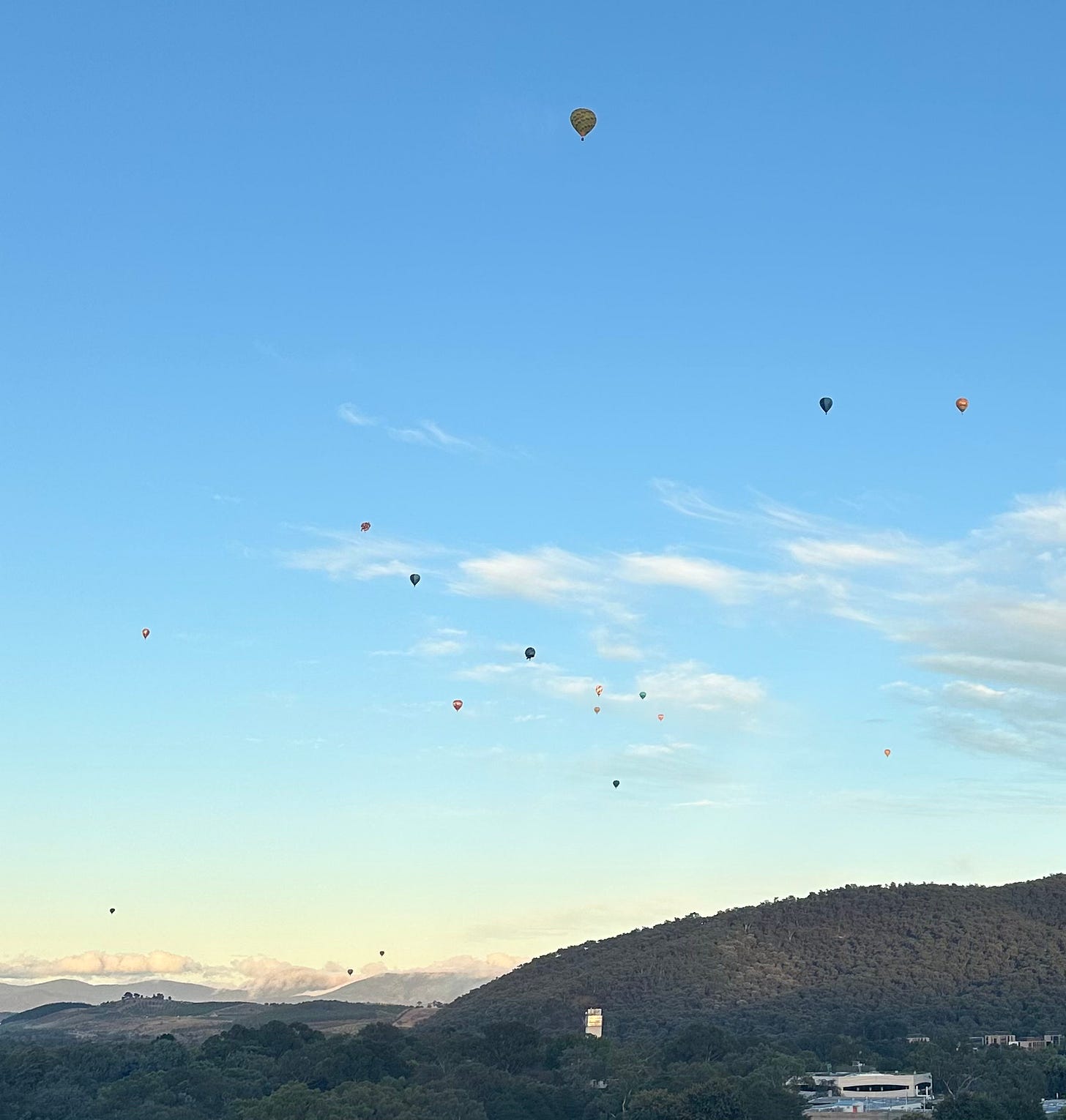 Hot air balloons fly over a hilly, green landscape