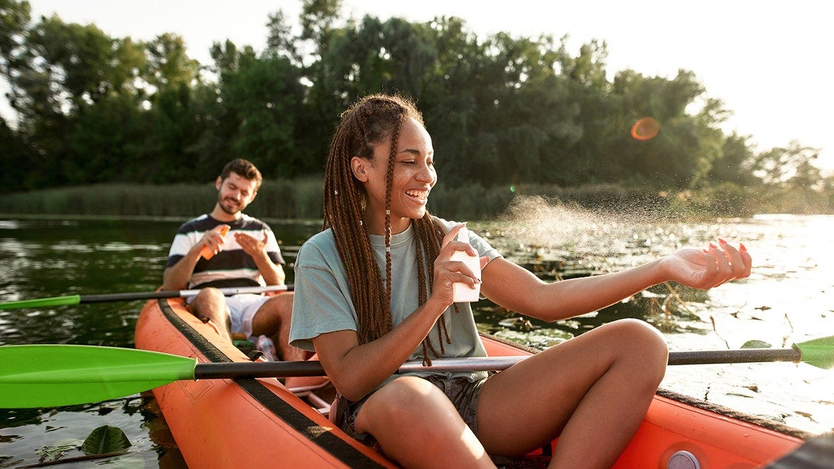 woman and man spraying sunscreen in a kayak