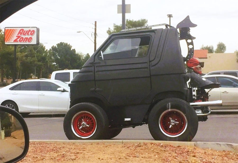 Photo of a highly modified black micro car with huge wheels, 'Mad Max' style accessories, including a fake skull that's painted red and wearing offroad goggles