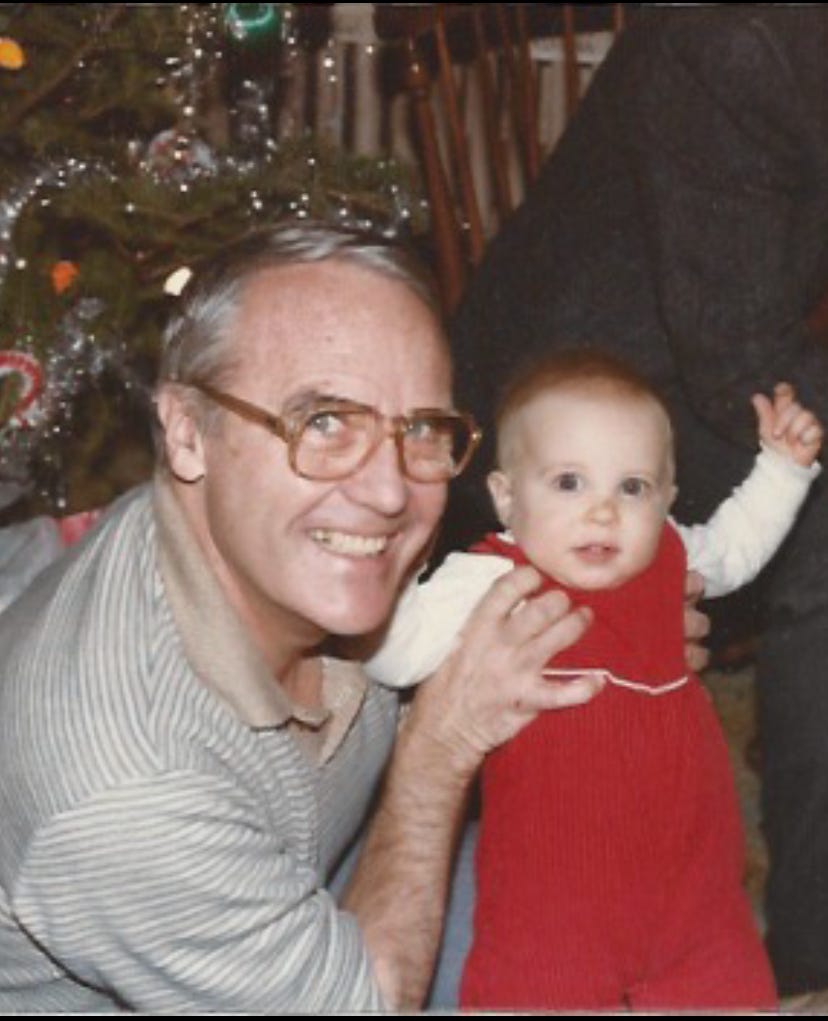 old man in glasses holds an infant in front of a christmas tree