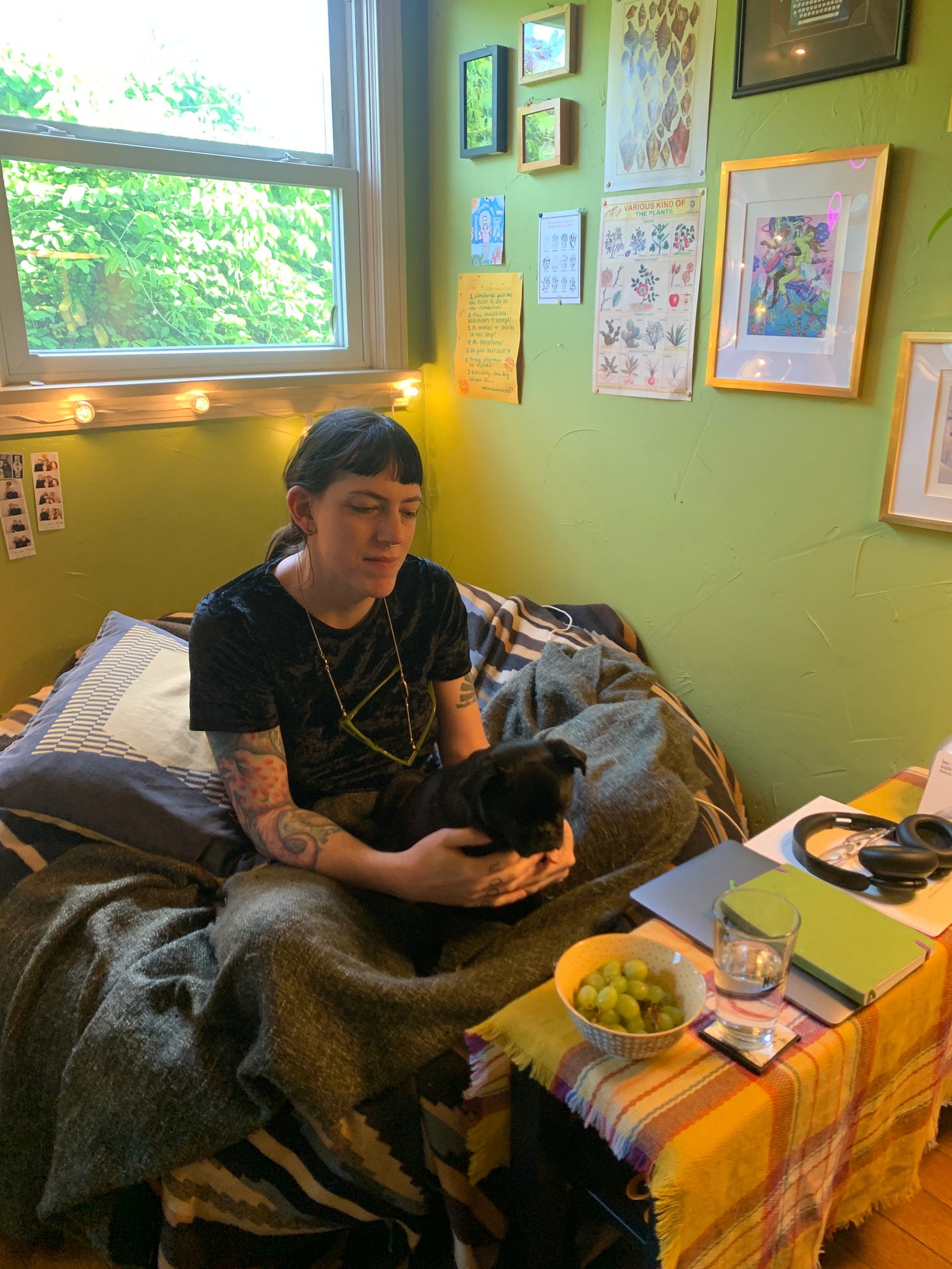 Emme sits on a bean bag chair in the corner of her writing studio. Her black pug sits on her lap. 