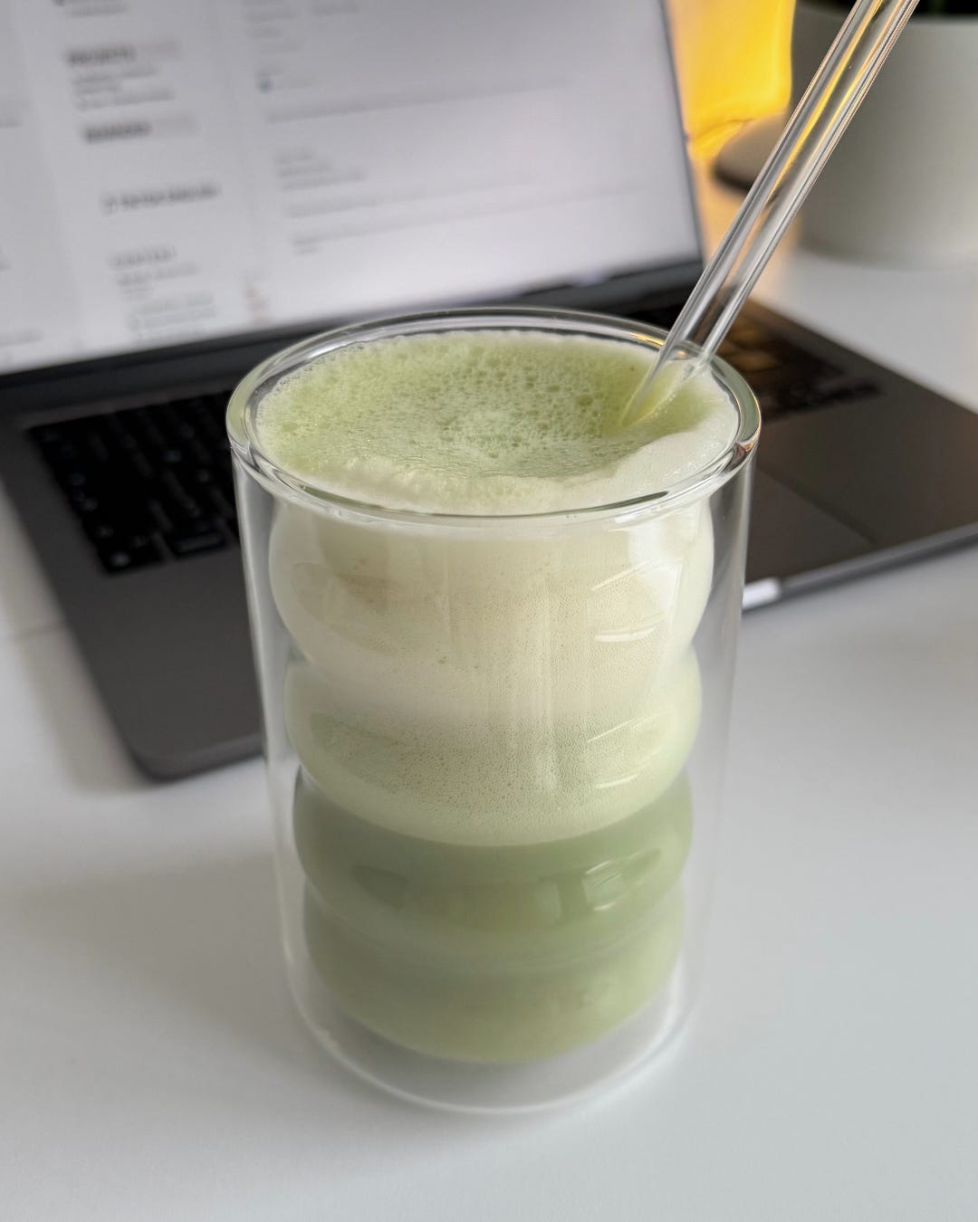 A beautifully frothed vanilla matcha latte with a sprinkle of matcha powder on top, next to a spoon and a small sifter.